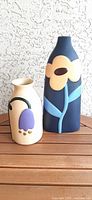 Photo showing two ceramic vases side by side with retro floral designs, one tall navy blue and one shorter cream colored