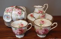 Front view of stacked teacups, saucers and side plates with cream jug on top showing floral design and gold trim