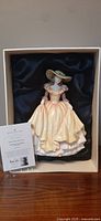 Porcelain figurine of a lady in a peach dress and wide-brimmed hat in original box with satin lining.