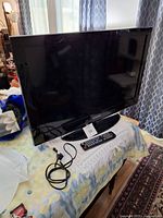 Samsung 32 inch TV on table with remote and power cable in front