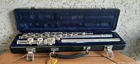 Full view of the silver metal flute disassembled inside the black hard case with blue velvet interior.
