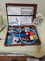 Wooden case open to show punch needle tool, embroidery hoops, colorful threads, manuals, and small accessories arranged inside.