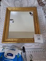 Front view of small rectangular mirror with ornate gold frame, reflecting ceiling and a wall.