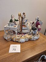 Overall view of the porcelain figural group showing three musicians: man at spinet, woman with harp, and seated gentleman, on ornate base with gold accents.