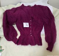 Top view of the deep purple angora sweater laid flat showing button-up front and puffed long sleeves with ribbed cuffs.