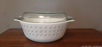 Front view of white Pyrex casserole dish with a clear glass lid, showing the tulip flower pattern on the side.