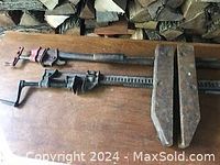 Three vintage wood clamps laid on a wooden surface with firewood in background, showing condition and style of clamps.