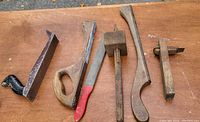 Six antique hand woodworking tools laid out on a wooden surface showing various saws, a scraper and marking gauges.
