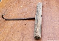 Antique hay hook lying flat showing the wooden handle with iron hook extending perpendicular from the center.