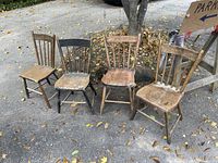 Front view of four antique pine chairs with two showing natural finish, one black painted, on outdoor ground with scattered leaves