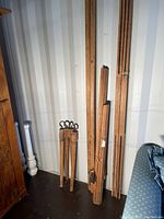 Disassembled antique quilt rack components leaning against the wall including vertical rods, stretchers and clamp mechanisms, showing wood finish and construction details.