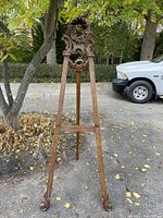 Full front view of carved wooden tripod easel standing outdoors showing decorative crest and legs