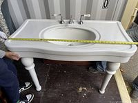 Full view of large white porcelain bathroom sink with chrome taps and four pedestal legs, tape measure showing width