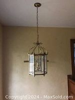 Front view of the antique brass hanging light suspended from ceiling with chain, showing glass panels and bulb arrangement.