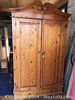 Front view of closed armoire showing carved scroll pediment and paneled doors