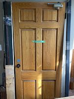 Full view of the exterior oak door, showing all six panels, door closer installed on top, and door knob with lockset.
