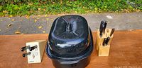Black speckled metal oven roaster with lid and block of knives inside