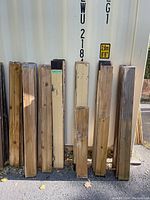 Photo showing 9 antique V groove pine wood boards leaning against a container, some painted cream/beige, others natural wood color, in fair condition with visible wear.