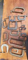 Photo showing full collection of 13 various metal C-clamps of different sizes on a wooden surface