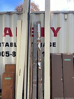 Wooden pine trim pieces and cardboard packaging against a white storage container outdoor.