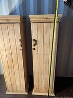 Front view of two matching tall wooden cabinets side by side, showing height with measuring tape, door and drawer details.