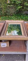Front view of the vintage gold framed mirror reflecting outdoor greenery.