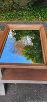 Top view of a rectangular mirror reflecting the sky and trees with a natural wood frame.