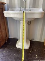Photo of the front of the white ceramic pedestal sink with tape measure showing height approx 31 inches.