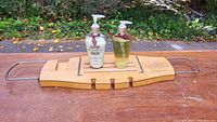 Wooden bamboo bathtub shelf with metal handles on either side, holding two pump bottles of liquid hand soaps placed on a wooden surface.