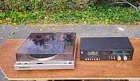 Photo showing Marantz turntable with clear dust cover and Technics cassette player side by side on a wooden surface outdoors.
