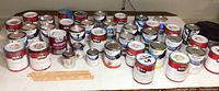 Wide view of 35 cans of various house paints, mostly quart sizes, multiple brands and colors, all on a table.