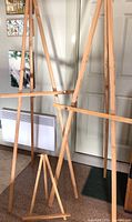 Three wooden easels shown standing indoors, two tall easels in background and smaller tabletop easel in front