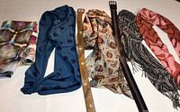 Overview of 5 scarves and 2 belts laid out horizontally on surface showing patterns and colors