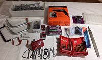Overview of lot including Black & Decker drill in box, assorted hand tools, hardware hooks, staples, drill bit sets, and file.