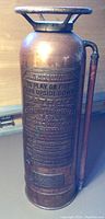 Front view of antique copper fire extinguisher showing embossed patent text and handle