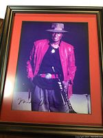 Framed autographed photo of Miles Davis in red jacket holding trumpet against dark background