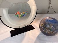 Tall, crescent-shaped frosted glass vase on black stand, with colorful marbles inside clear center area.