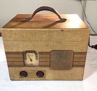 Front view of the vintage Philco radio and turntable unit in its textured brown and tan carrying case with a leather handle on top. Shows speaker grill, radio dial, and control knobs.