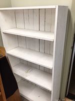 Tall white wooden shelf with three shelves and vertical slat back, showing distressed paint and wear marks