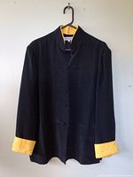Black silk coat with sunflower yellow cuffs and collar lining, shown on hanger.