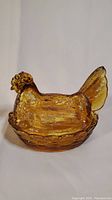 Amber glass hen in basket, showing front and tail of hen with textured feathers and translucent amber color.