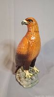 Front view of ceramic whisky decanter shaped like a golden eagle perched on a rock base