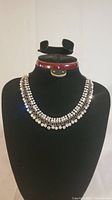 Full front view of rhinestone necklace on black display bust showing two rows of rhinestones and darker metal setting with chain link detail.