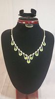 Full view of the delicate rhinestone necklace displayed on a black bust, showing the overall design with green and clear stones.