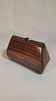 View of the trapezoidal wooden small change purse showing smooth polished dark wood grain and carved clasp.