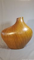Full view of large abstract rounded vase with narrow neck covered in teak wood strips.
