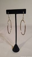 Front view of the large oval sterling silver hoop earrings hanging on hooks, displayed on black stand.