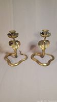 Pair of brass cobra candle holders shown front view against white background