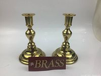 Front view of both brass candlesticks showing shape and finish with a 'BRASS' label in front.