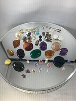 Overview of assorted gems, stones, beads, pearls, and jewelry components spread on a reflective surface showing colors, shapes, and sizes.